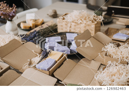 Handmade lavender soaps packed in kraft boxes with shredded filler in a cozy workspace. Home-based business, handmade skincare, small batch production, eco-friendly packaging 126982463
