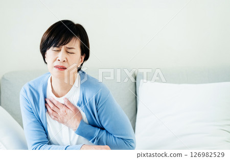 Middle-aged woman sitting on sofa with hands on chest 126982529