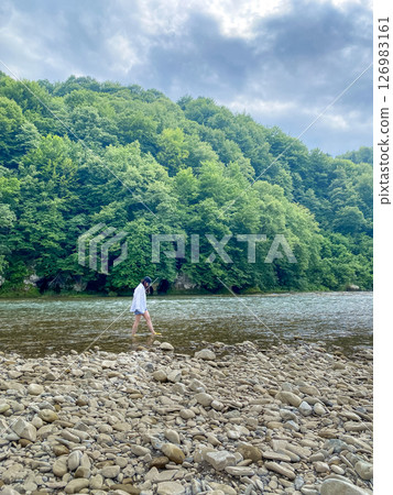 Person Walking Along Riverbank in Lush Forest 126983161