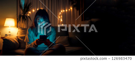 Woman in bed at night, scrolling on her smartphone, illustrating FOMO, fear of missing out, or watching a movie. A woman captivated by her smartphone while in bed at night, perhaps scrolling 126983470