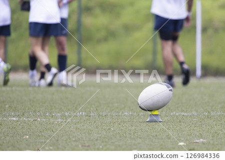 Rugby ball standing on kicking tee on field with players training 126984336