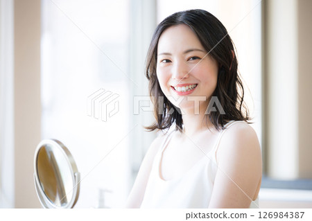 Cosmetics and beauty image of a young woman with beautiful bare skin taking care of herself while looking in the mirror, close-up, looking at the camera 126984387
