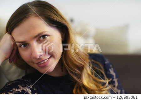Candid portrait of young woman with long hair, leaning her head on hand, blurred background 126985061