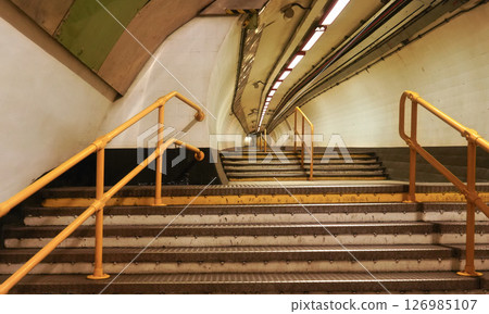 Stairs leading into tunnel illuminated by neon lights inside London underground train station Stairs leading into tunnel illuminated by neon lights inside London underground train station 126985107