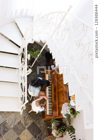 Two young women enjoy a piano duet near a white staircase. Sunlight streams in, illuminating the scene. Two young women enjoy a piano duet near a white staircase. Sunlight streams in, illuminating the scene. 126986444