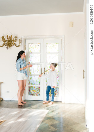 A mother and son playfully interact inside their home, the boy holding a long stick playfully. A mother and son playfully interact inside their home, the boy holding a long stick playfully. 126986445