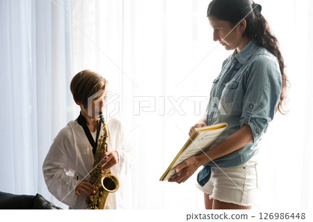 A boy practices the saxophone with his mother's guidance, showcasing a heartwarming musical lesson. 126986448
