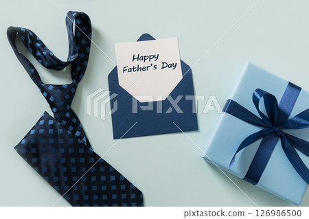 Greeting card with blue gift, necktie, sheet on blue background. Men's accessories set. Top view. Copy space. Happy Fathers Day - text. 126986500