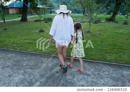 A woman and child stroll hand-in-hand through a park, enjoying a sunny afternoon. 126986520