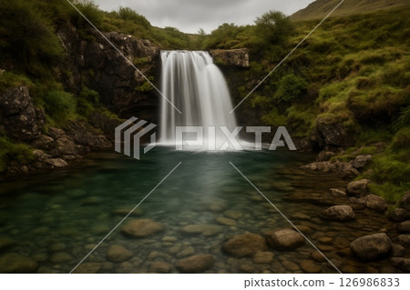 Mountain waterfall flowing into rocky pool surrounded by green hills and vegetation under cloudy sky in natural landscape Mountain waterfall flowing into rocky pool surrounded by green hills and vegetation under cloudy sky in natural landscape 126986833