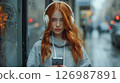 A young woman in a gray hoodie and white headphones on a city street. 126987891