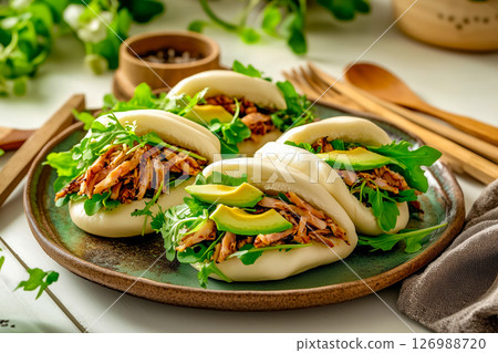Vegan bao buns filled with jackfruit, avocado, and mixed greens, served on a rustic ceramic plate with wooden utensils, creating a fresh and natural dining presentation 126988720
