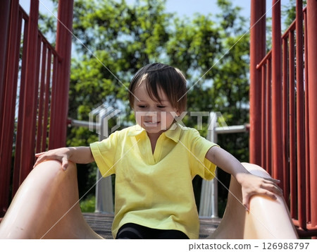 portrait of a smiling little brunette boy in a yellow T-shirt playing outdoors. happy child, lifestyle. products for children. little boy playing in playground 126988797
