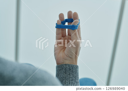 man exercises his fingers with a blue elastic band 126989040