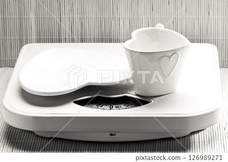 Empty plate saucer and mug cup on weighing scale. 126989271