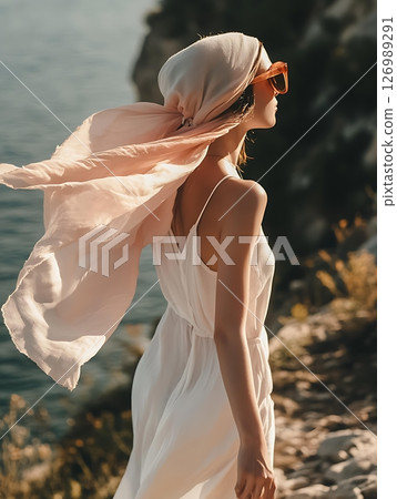 Elegant woman in sunglasses on a cliff by the sea, chic summer fashion, windswept hair, breathtaking ocean view, golden hour glow 126989291
