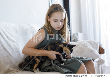 Cheerful young girl hugging her cat pet sitting on cosy sofa, relaxing at home. Cheerful young girl hugging her cat pet sitting on cosy sofa, relaxing at home. 126989549