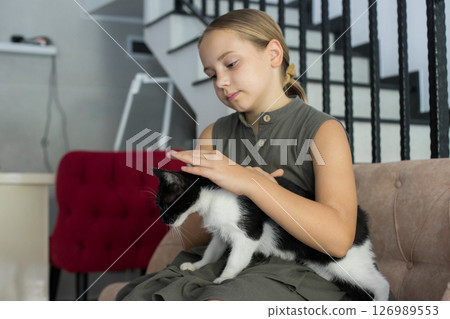 Pretty child girl bonding playful furry cat pet companion sitting on cosy sofa indoor 126989553