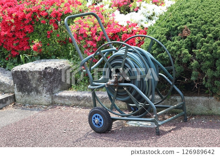 Landscape with a wheeled hose reel for watering in a flowered park Landscape with a wheeled hose reel for watering in a flowered park 126989642