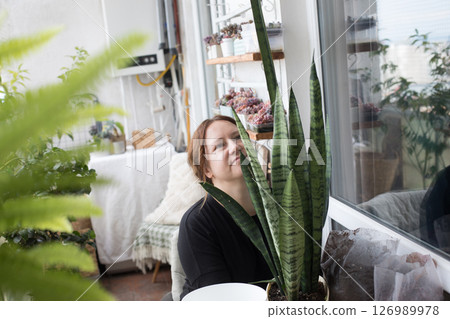 Pretty mid adult woman holding green houseplant in her hand standing indoor. Pretty mid adult woman holding green houseplant in her hand standing indoor. 126989978