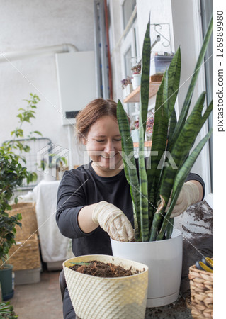 Attractive mid adult woman holding green houseplant in her hand standing indoor.  126989980