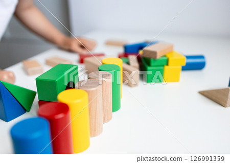 Colorful wooden blocks on white table with child hand in background 126991359