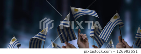 Uruguay flags in their hands on a blurred urban background Uruguay flags in their hands on a blurred urban background 126992651
