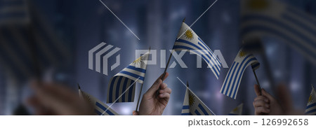 Uruguay flags in their hands on a blurred urban background 126992658