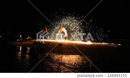 Fire dancers performing at night on the beach with sparks flying 126993155
