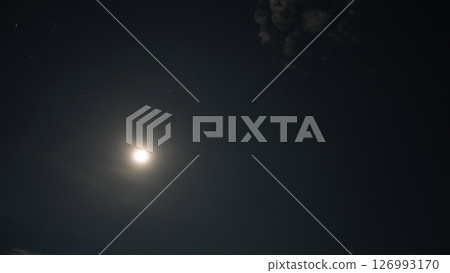Bright moon shining through scattered clouds in night sky 126993170