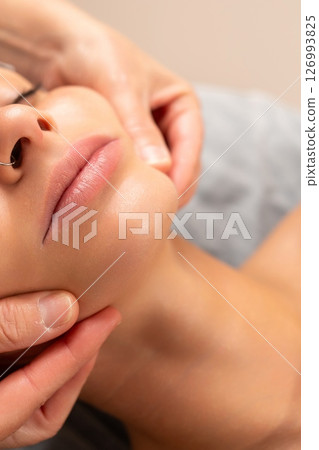 Close-up of a facial massage session, with hands gently massaging a woman s chin and jawline. 126993825