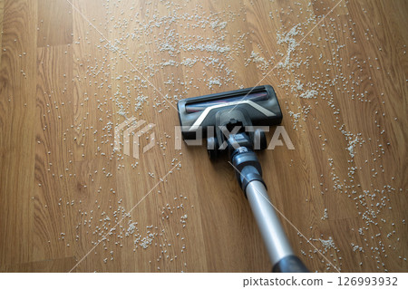 Vacuum cleaner nozzle picking up scattered rice grains from a wooden floor concept of cleaning, mess, and home maintenance. Vacuum cleaner nozzle picking up scattered rice grains from a wooden floor concept of cleaning, mess, and home maintenance. 126993932
