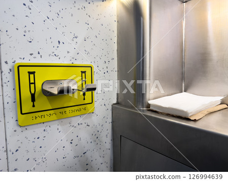 Wall mounted crutch holder with tactile braille sign in a public restroom for people with disabilities. Focus on inclusive urban design, accessibility, and thoughtful infrastructure 126994639