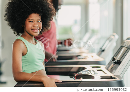 Portrait happy smiling African black healthy kid, Girl child at fitness sport club treadmill machine Portrait happy smiling African black healthy kid, Girl child at fitness sport club treadmill machine 126995082