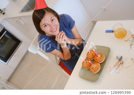 Woman celebrates with four cupcakes topped with candles in place of traditional birthday cake. Smiling and joyful, he enjoys cozy and unique celebration, creating warm and memorable festive moment. Woman celebrates with four cupcakes topped with candles in place of traditional birthday cake. Smiling and joyful, he enjoys cozy and unique celebration, creating warm and memorable festive moment. 126995390