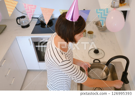 Young woman celebrates her birthday at home, surrounded by cozy atmosphere and festive decorations. She cooking a festive dinner, delicious pasta 126995393