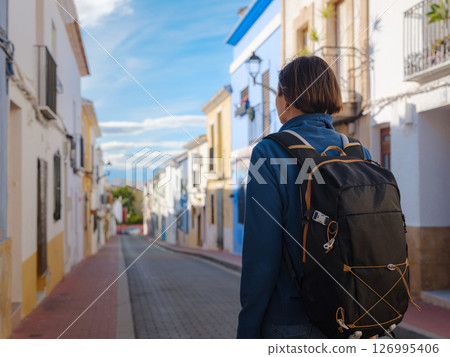 Young woman strolling through charming narrow streets of Denia, Alicante province, Spain, surrounded by historic Mediterranean architecture , enjoying peaceful atmosphere and cultural ambiance. 126995406