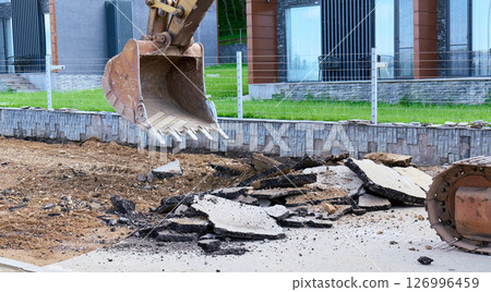 Heavy machinery lifts broken pavement at a residential area 126996459