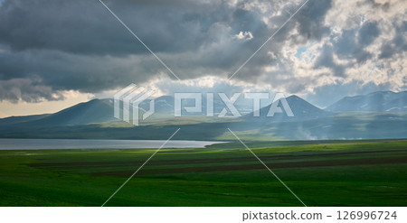 Sunlight breaks through clouds over serene mountains and a calm lake. High quality photo 126996724