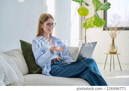 Young teenage girl using laptop for video chat sitting on sofa at home Young teenage girl using laptop for video chat sitting on sofa at home 126996771