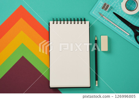 A blank sketchbook page with paper craft supplies in the background. Turquoise background, space for your text. 126996805