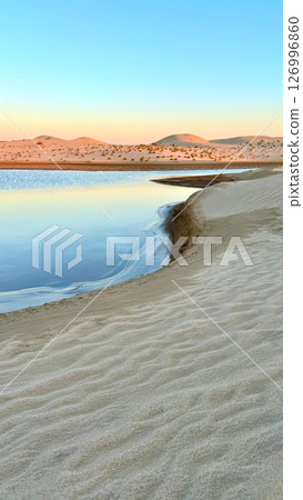 Lake cuts through dry desert terrain with salty surface glowing under sunset sky, where desert erosion sculpts basin and salty water gives lake a rare ecological character. 126996860