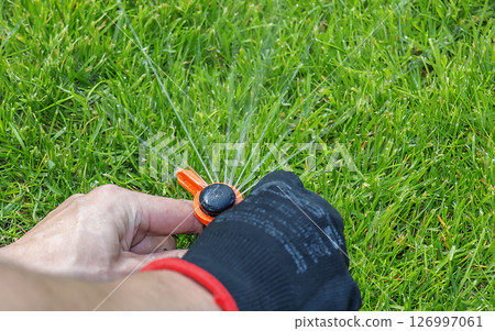 A gardener's gloved hand adjusts a sprinkler to water the lawn, keeping the grass in good condition. A gardener's gloved hand adjusts a sprinkler to water the lawn, keeping the grass in good condition. 126997061