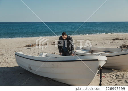 Man At The Beach Examining A Boat Man At The Beach Examining A Boat 126997399