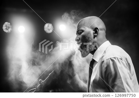 Soloist at microphone during concert in jazz club, soloist in clouds of stage smoke performs jazz, copy space with concept of performances during jazz festival, black and white vintage style shot 126997750