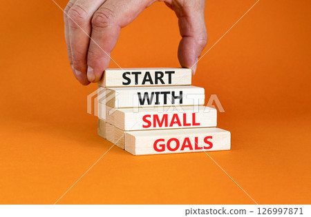 Start with small goals symbol. Concept words phrase Start with small goals on beautiful wooden blocks. Beautiful orange background Businessman's hand Business Start with small goals concept Copy space 126997871