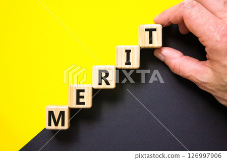 Merit symbol. Concept word Merit on beautiful wooden blocks. Beautiful yellow and black background. Businessman hand. Business lifestyle merit concept. Copy space. Merit symbol. Concept word Merit on beautiful wooden blocks. Beautiful yellow and black background. Businessman hand. Business lifestyle merit concept. Copy space. 126997906