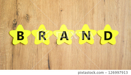 Brand symbol. Concept word Brand on beautiful yellow paper stars. Beautiful wooden table wooden background. Business brand concept. Copy space. 126997913