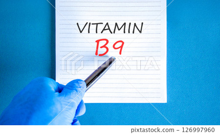 Vitamin B9 folic acid symbol. Concept words Vitamin B9 on beautiful white note. Doctor's hand in blue medical glove. Beautiful blue background. Medical healthy lifestyle Vitamin B9 concept. Vitamin B9 folic acid symbol. Concept words Vitamin B9 on beautiful white note. Doctor's hand in blue medical glove. Beautiful blue background. Medical healthy lifestyle Vitamin B9 concept. 126997960