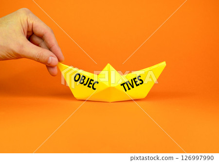 Objectives symbol. Concept word Objectives on beautiful yellow paper boat. Beautiful orange background. Businessman hand. Business objectives concept. Copy space. 126997990
